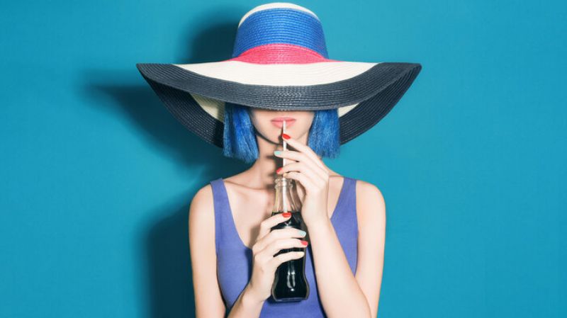 Young woman in hat drinks soda